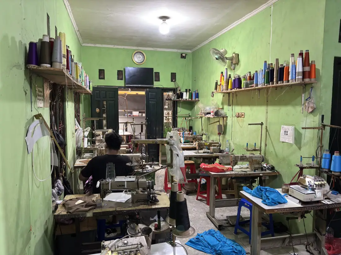 Ruang jahit workshop dengan deretan mesin dan rak benang